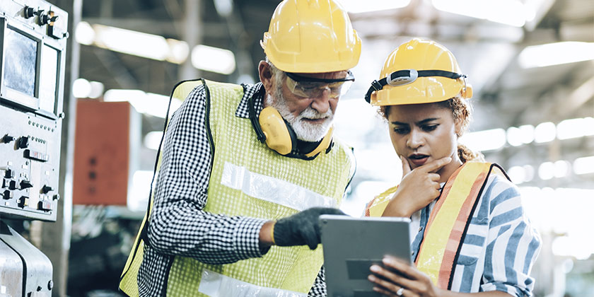 dois colaboradores usando os EPIs devidos olhando em um tablet para saber quais atividades de gestão de facilities devem ser realizadas