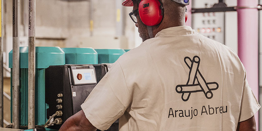 Homem com o uniforme da Araujo Abreu e usando os EPIs corretamente realizando manutenção preventiva no maquinário da empresa.