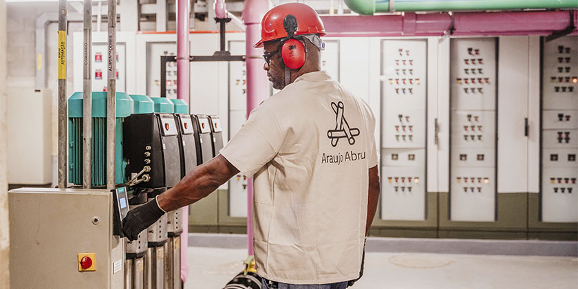 Homem de capacete e uniforme da Araujo Abreu fazendo manuteção em uma máquina.