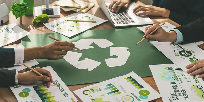 Empresários em reunião discutindo ações para aumentar a sustentabilidade nas práticas da empresa com um símbolo da reciclagem no centro da mesa.