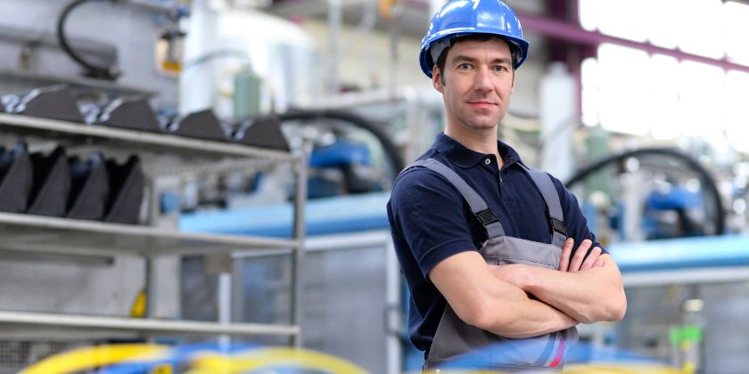 Engenheiro de braços cruzados em uma fábrica, demonstrando sua capacitação profissional.