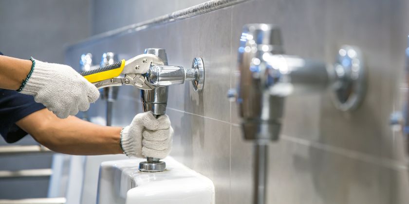 Encanador realizando a manutenção preventiva de torneiras para aumentar a eficiência hídrica de um edifício.